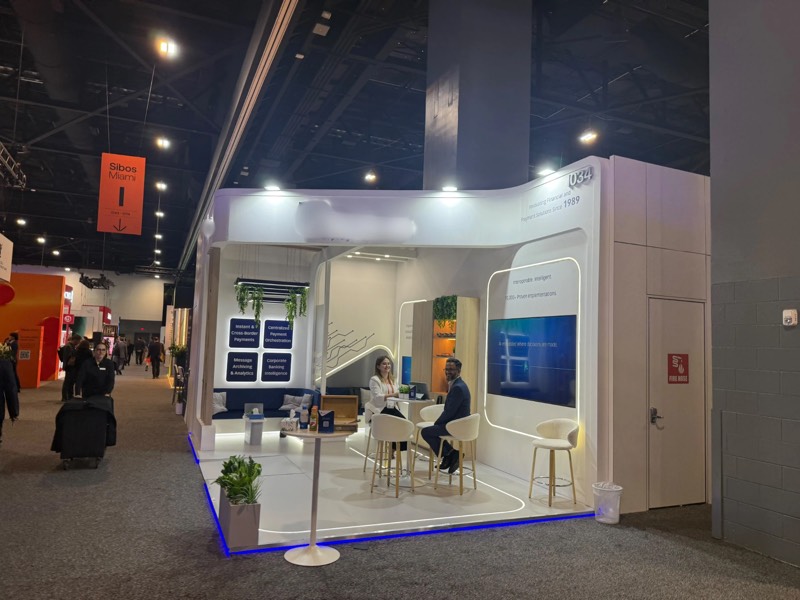 Meeting area with LED screen and navy lounge seating inside the white curved-wall stand at SIBOS 2026, Miami
